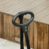 A close-up of a black stroller handle with a black strap attached, set against a wooden background. Produktbild-Vorschau