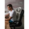 A man is sitting at a desk using a laptop, with a massage cushion attached to his office chair. Produktbild-Vorschau