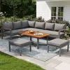 An outdoor patio set with a sectional sofa, coffee table, and ottomans on a rug, with a house and garden in the background. Voir les images du produit