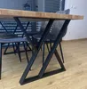 A close-up view of a dining table with black metal legs and a wooden tabletop, with chairs visible in the background. Anteprima dell’immagine prodotto