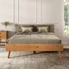 A bed with wooden frame and gray headboard, dressed with bedding and pillows, in a room with decorative wall molding and a window with greenery outside. Produktbild-Vorschau
