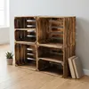Four wooden crates stacked in a corner against a wall, with a plant and books nearby. Náhled obrázku produktu
