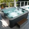 A hot tub filled with bubbling water on a wooden deck, surrounded by lush greenery and a white railing. Náhľad obrázku produktu