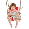 A young child with red hair is sitting in a baby swing. The swing has a red and white striped fabric seat and wooden bars. The child is wearing a blue and green patterned swimsuit with flamingos on it. Produktbild-Vorschau