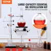 A distillation kit for essential oils is displayed on a wooden table, with various accessories and bottles arranged around it. The background is a light gray wall with some decorative elements. Produktbild-Vorschau