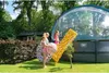 Three young girls are standing on a grassy lawn next to a large round swimming pool with a transparent dome cover. They are holding inflatable pool toys, including a leopard-print ring and two large leopard-print balls. A yellow inflatable mat with a leopa Produktbild-Vorschau