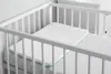 A white baby pillow with teal trim is placed inside a white crib. Anteprima dell’immagine prodotto