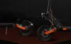 Close-up view of the rear wheel and suspension system of an electric scooter, with a dark, textured background. Náhled obrázku produktu