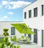 An outdoor patio scene with a table and chairs set up under a large green umbrella, next to a modern white building. Produktbild-Vorschau
