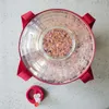 A top-down view of a fermentation vessel filled with a pinkish mixture, with a red lid and straps visible. Produktbild-Vorschau