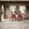 An outdoor dining set with red chairs and a white table on a stone patio, under a tiled roof. Voir les images du produit