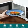 A hand is placing a plate of food into a microwave. Voir les images du produit