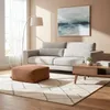 A living room scene with a sofa, ottoman, coffee table, and artwork. Produktbild-Vorschau