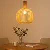 A wooden pendant lamp hangs above a wooden table with a vase of greenery, a mug, and a book. Voir les images du produit