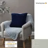 A dark blue pillow and a light blue blanket are draped over a beige armchair. Produktbild-Vorschau
