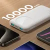 A white power bank with a wireless charging pad is shown on a wooden surface, surrounded by smartphones. Produktbild-Vorschau