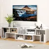 A modern living room setup featuring a white modular TV stand with various decorative items and a large flat-screen television displaying a scenic landscape. Náhled obrázku produktu