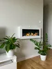 A modern living room with a white ethanol fireplace mounted on a light gray wall, flanked by two potted plants. Anteprima dell’immagine prodotto