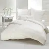 A neatly made bed with white bedding and pillows, next to a small white nightstand with vases of white flowers. Produktbild-Vorschau