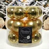 A clear plastic container filled with gold Christmas ornaments, set against a backdrop of snowy Christmas trees. Produktbild-Vorschau