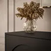 A close-up shot of a black dresser with a glass vase of dried flowers on top. Produktbild-Vorschau