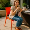 A woman is sitting on an orange chair at a table outdoors, holding a glass of white wine. Voir les images du produit