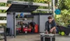 A man is organizing tools and equipment inside and around an open storage shed in an outdoor setting. Anteprima dell’immagine prodotto