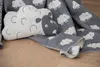 A close-up shot of a sheep-themed blanket and pillow on a wooden floor. Produktbild-Vorschau