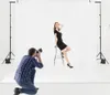 A photographer is taking a picture of a model in a studio setting with a white backdrop and lighting equipment. Náhľad obrázku produktu