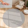 A round, light gray rug is placed on a wooden floor in a living room setting, with a chair and a pouf nearby. Produktbild-Vorschau