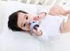 A baby lying on a white surface, chewing on a blue teething toy. Voir les images du produit