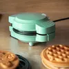 A mint green mini waffle maker is placed on a wooden surface, with two waffles in the foreground. Náhled obrázku produktu
