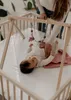 A baby is lying on a play mat inside a wooden playpen, with a mobile hanging above. Produktbild-Vorschau