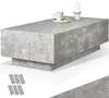 A rectangular coffee table with a concrete-like finish is shown against a white background. A coffee cup, a small plate with snacks, and a candle on a holder are placed on top of the table. Several small rectangular items, possibly floor protectors, are ar