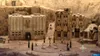 A miniature diorama of a town square with stylized buildings and small figures. Produktbild-Vorschau