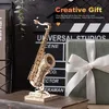 A wooden model of a saxophone is displayed on a table next to a gift-wrapped box and a movie clapperboard. Text overlays suggest it is a creative gift. Podgląd zdjęcia produktu
