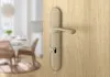 A close-up of a door handle on a wooden door, with a blurred background of a dining area. Produktbild-Vorschau
