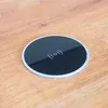 A round, black wireless charger with a silver rim sits on a wooden surface. Produktbild-Vorschau