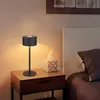 A black LED table lamp is placed on a wooden nightstand next to a tissue box and a bed. Náhľad obrázku produktu