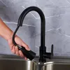 A hand is shown pulling the spray head of a black kitchen faucet over a stainless steel sink. Produktbild-Vorschau