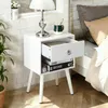 A white nightstand with an open drawer next to a bed. Náhled obrázku produktu