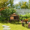 A rabbit hutch with an attached run is set up in a grassy backyard with a white picket fence in the background. Produktbild-Vorschau