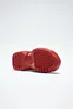 The underside of a red sneaker is shown against a white background. Voir les images du produit