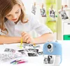 A young girl is coloring printed photos with markers, with a blue mini thermal printer in the foreground. Produktbild-Vorschau