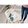 A person is using a handheld vacuum cleaner to clean up crumbs from a child's high chair. Produktbild-Vorschau
