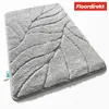 A close-up, angled view of a grey bath mat with a leaf pattern, placed on a white background. A logo is visible in the top right corner. Anteprima dell’immagine prodotto