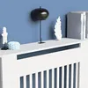 A white radiator cover with decorative items on top, set against a blue wall. Náhled obrázku produktu