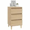 A light brown wooden bedside table with three drawers and tapered legs, decorated with framed pictures and a small potted plant on top. Náhled obrázku produktu