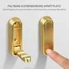 A folded and an unfolded brass hook on a white wall, with text overlay. Produktbild-Vorschau
