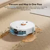 A white robot vacuum cleaner is shown on a wooden floor, cleaning up spilled liquid and debris. Produktbild-Vorschau